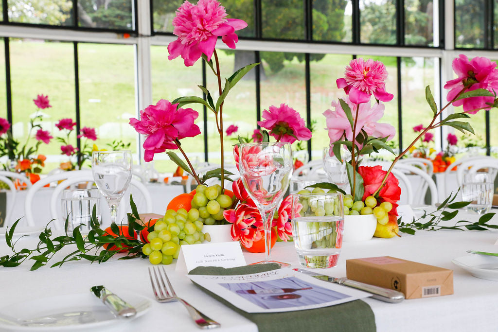 Elegant table setting with vibrant pink flowers, greenery, and fruit accents.