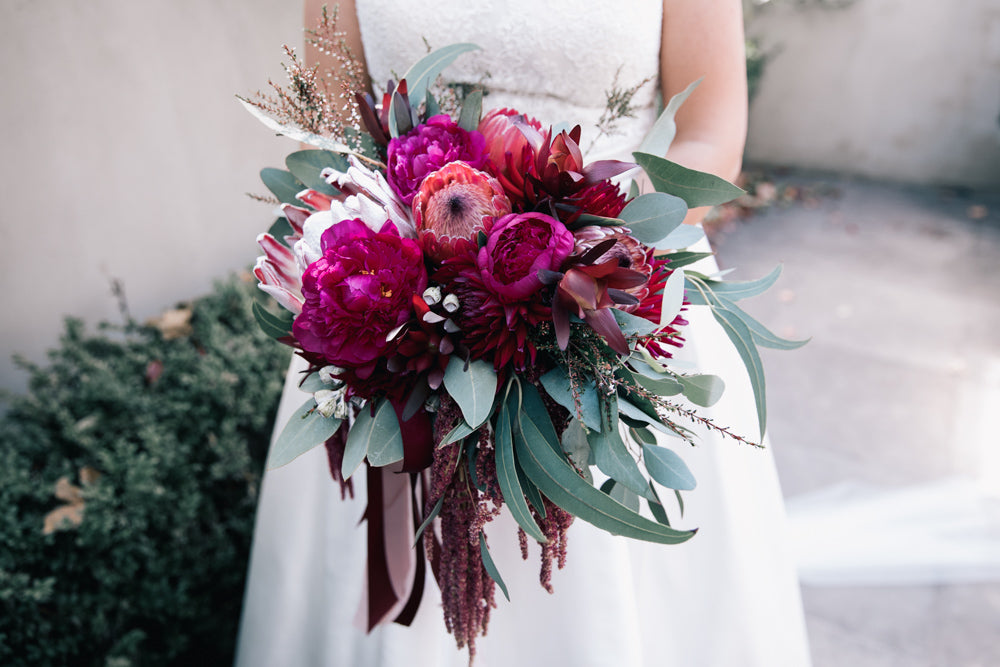 Bride holding a vibrant wedding bouquet with red and pink flowers.