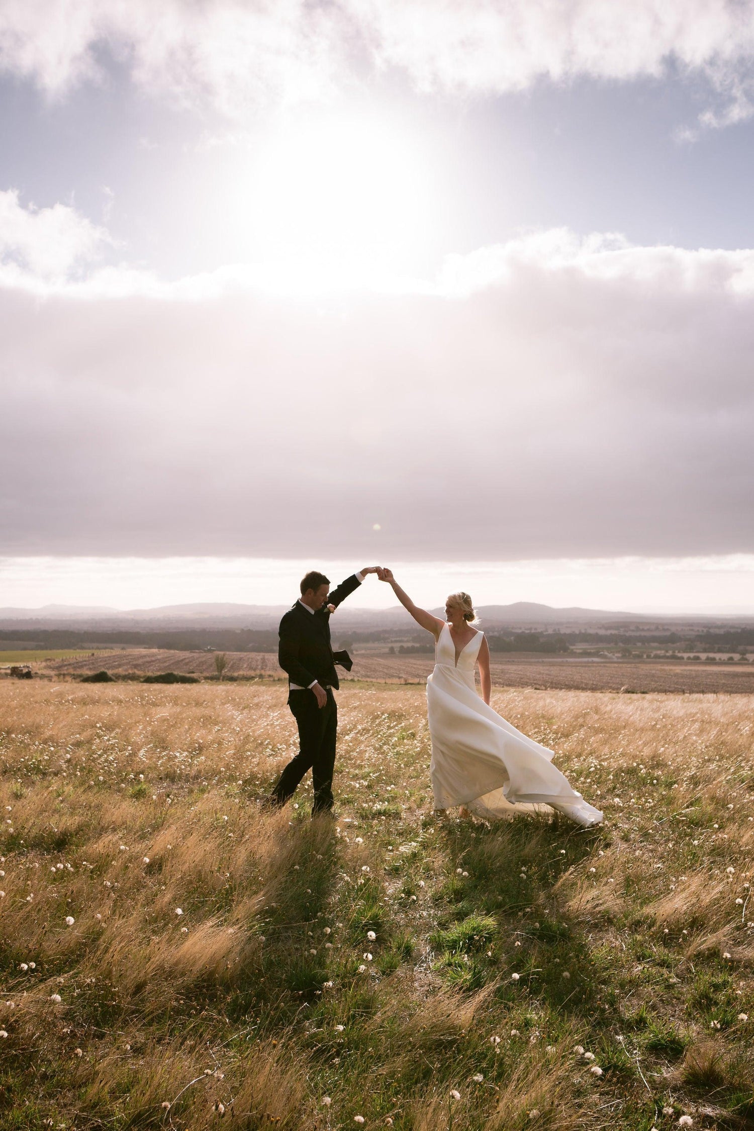 A couple holding hands in the sunlight with their wedding flowers