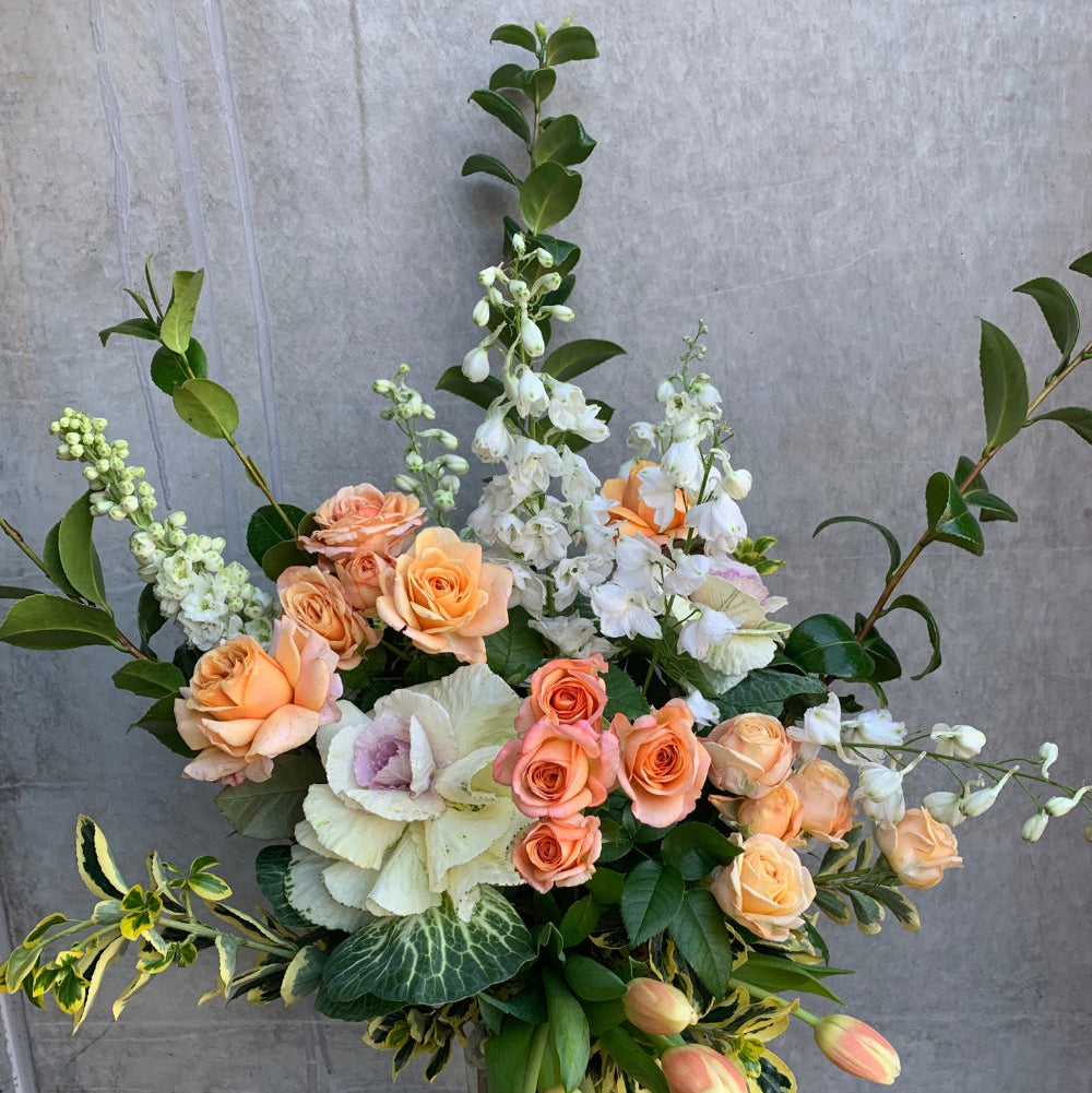 Elegant floral arrangement titled 'Peachy Love' featuring peach roses, white blooms, and lush greenery. Perfect for gift giving and celebrations.