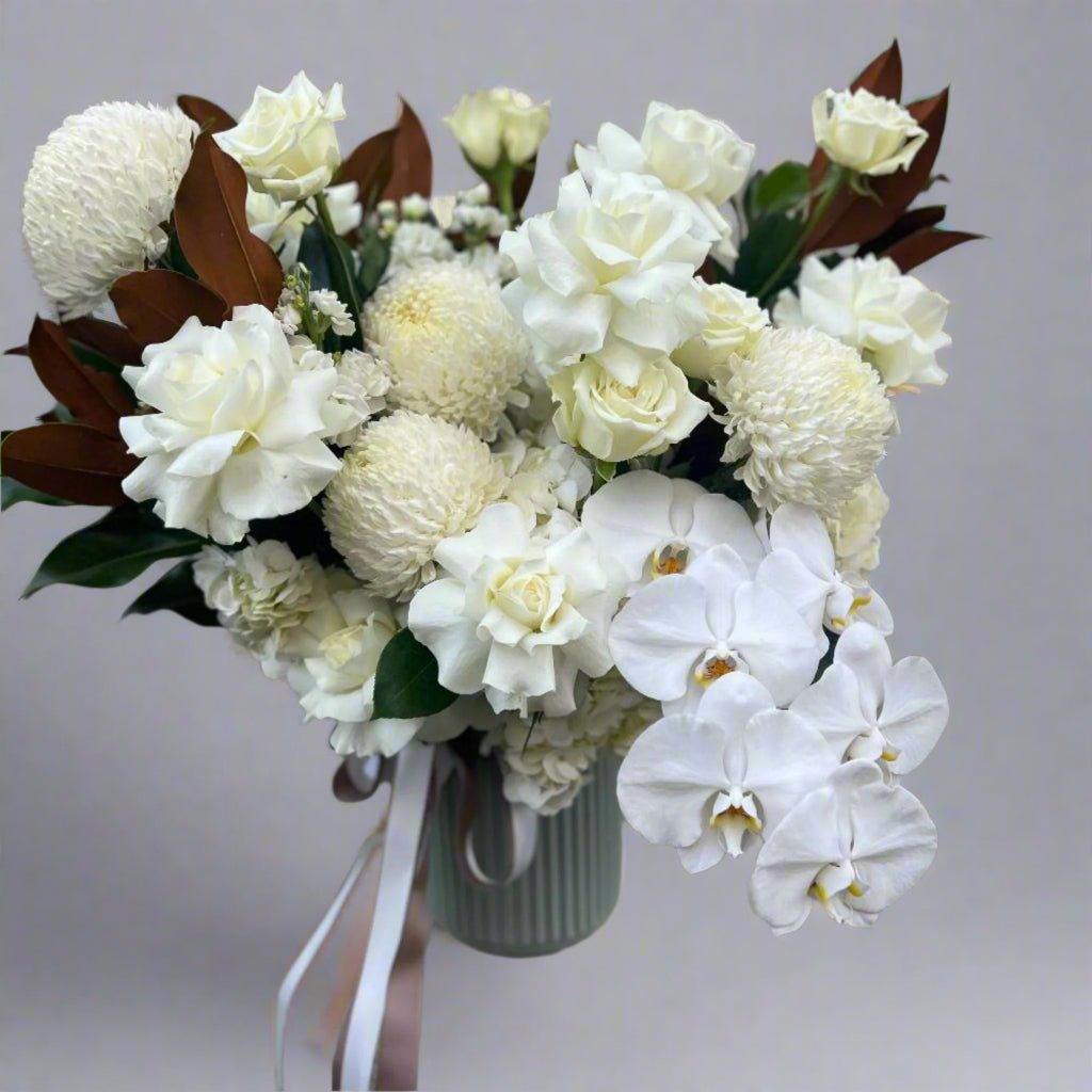 White orchids, white roses and white disbuds with foliage bouquet in grey vase