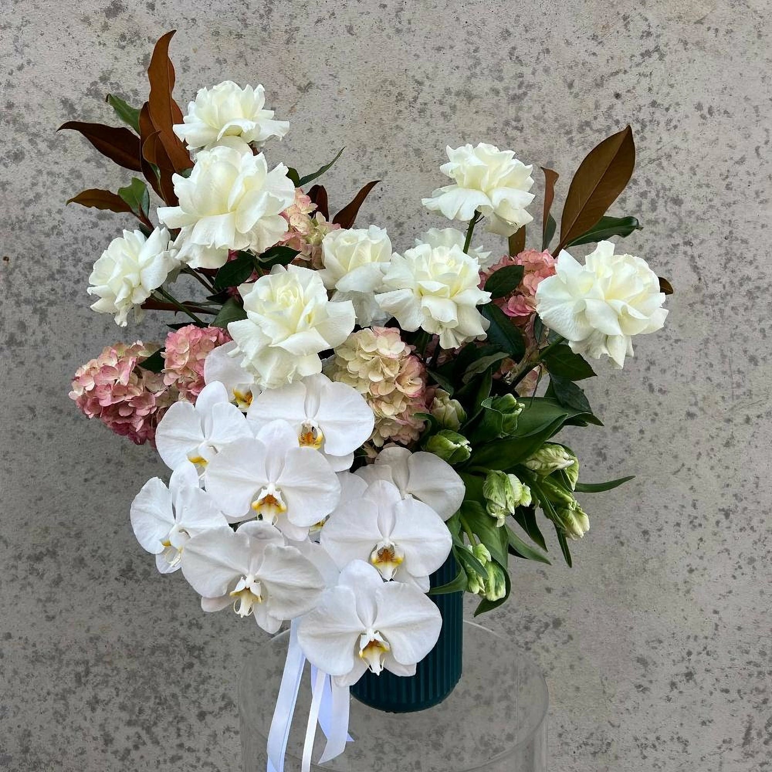 Elegant white rose bouquet with orchids and hydrangeas in a green vase, perfect for Valentine's Day gifting. Fresh and neutral floral arrangement.