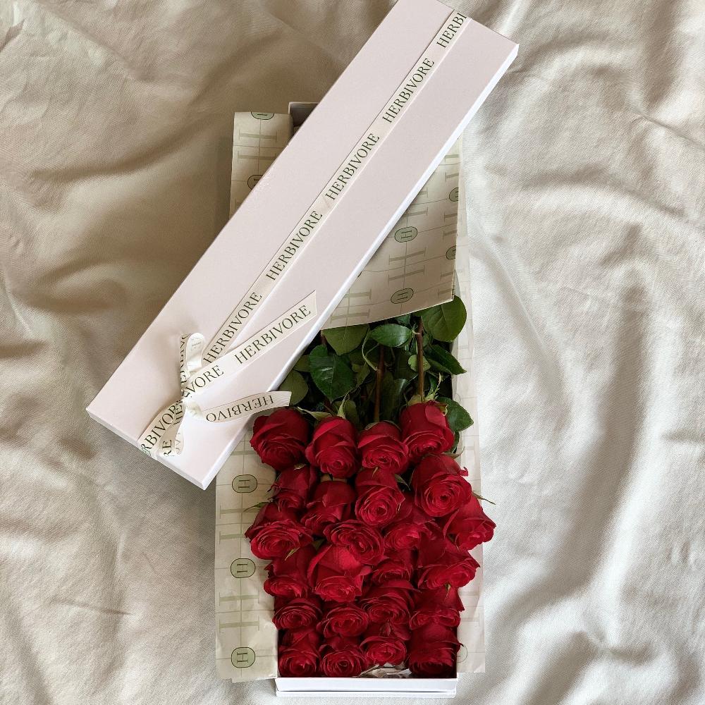 Two dozen premium long-stem red roses elegantly arranged in a signature gift box with branded wrapping, perfect for special occasions.