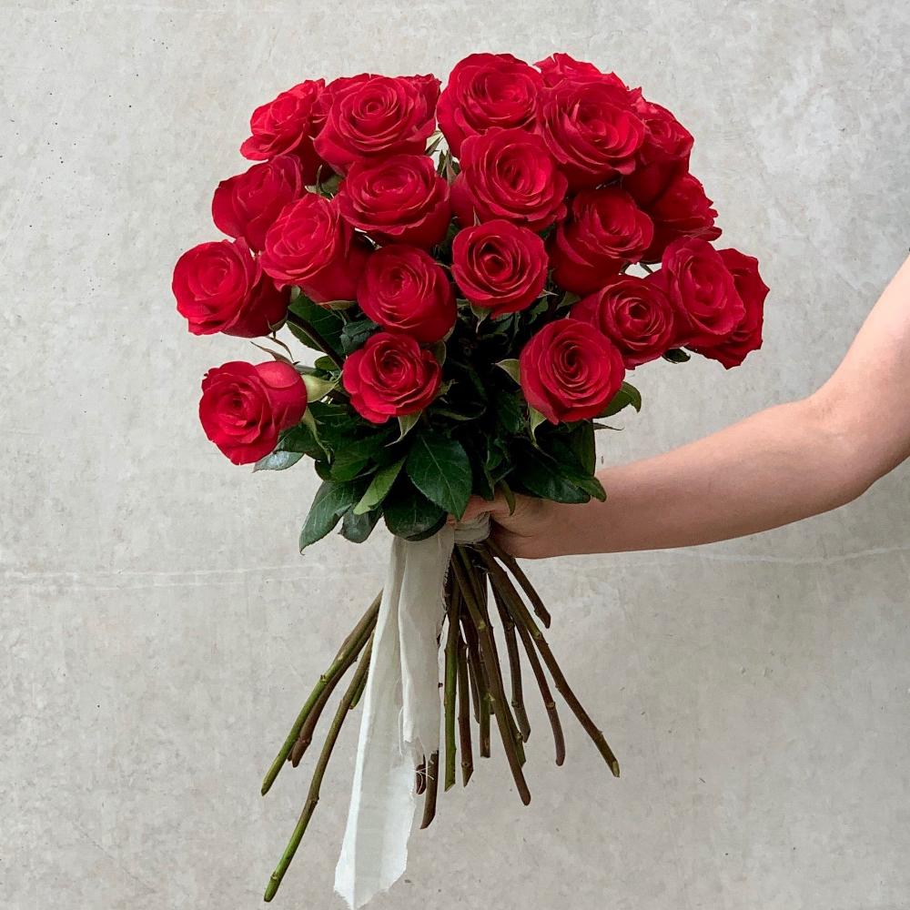 Hand-tied bouquet of twenty-four vibrant red roses with lush green stems, ideal for Valentine's Day or romantic gestures.