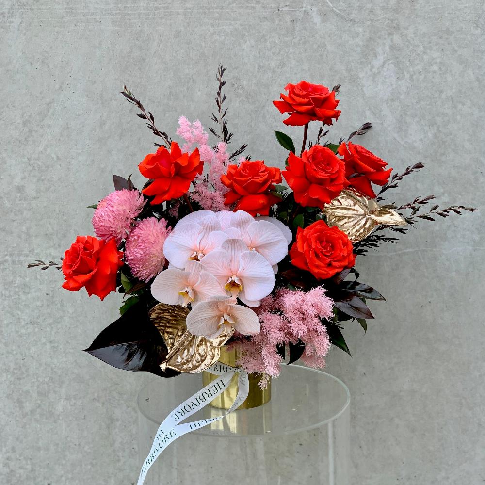 Elegant floral arrangement featuring red roses, pink orchids, and gold accents in a decorative vase. Perfect for Valentine's Day flower delivery in Melbourne.